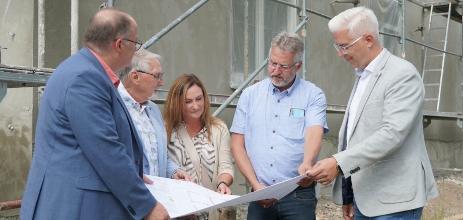 Fünf Personen stehen gemeinsam vor einem fast fertiggestellten Gebäude mit Gerüst – der künftigen Tagespflegeeinrichtung in Liers. Sie sind ins Gespräch vertieft. Zu sehen sind von links: Guido Nisius, Jürgen de Temple, Martina Romes, Uwe Szymanski und Dominik Gieler. Das Bild zeigt einen Moment des gemeinsamen Austauschs.